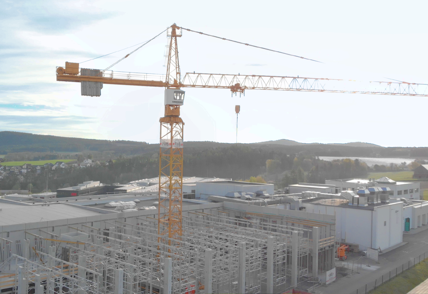 Drohnenaufnahme eines Krans, der mitten im Stahlgerüst einer Industriehalle steht